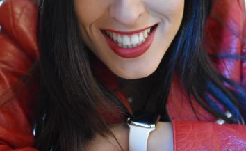 a girl smiling at the camera and wearing a red leather jacket.