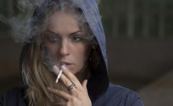 A girl in a hoodie smoking a cigarette.