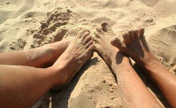 Two pairs of feet covered in sand.