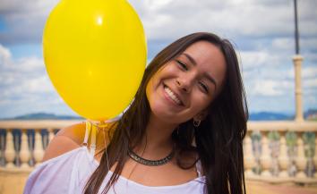 happy girl posing with her yellow balloon on a balcony.
