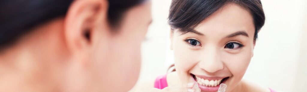 A woman looking at the mirror while holding her Invisalign aligners