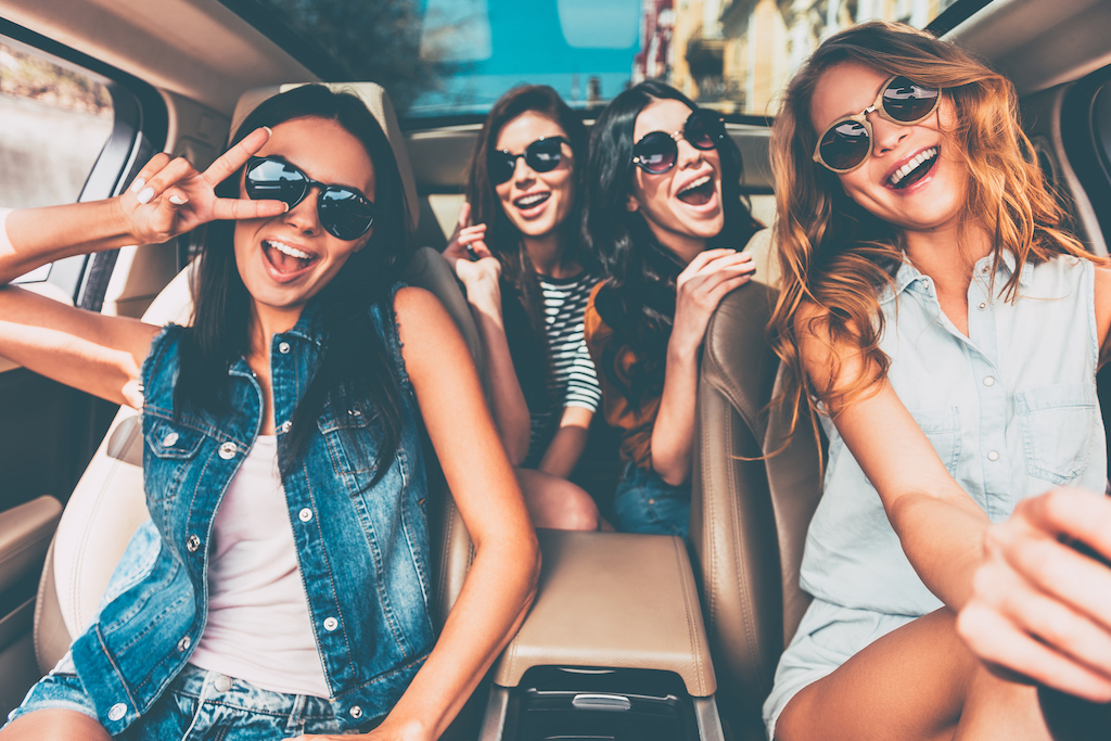 Four beautiful young cheerful women looking happy and playful while sitting in car