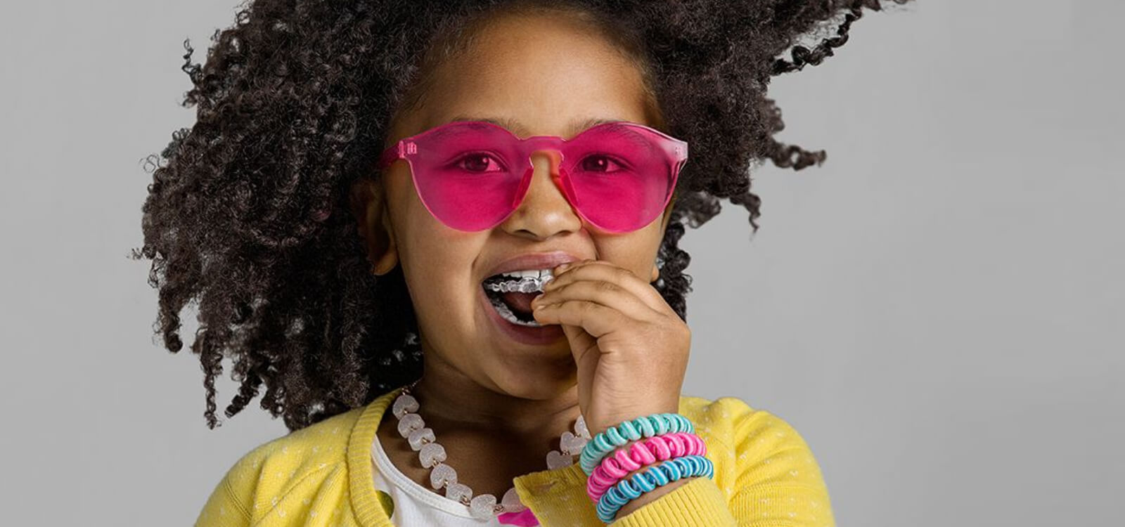 Little girl with modern sunglasses putting on her invisalign clear aligners