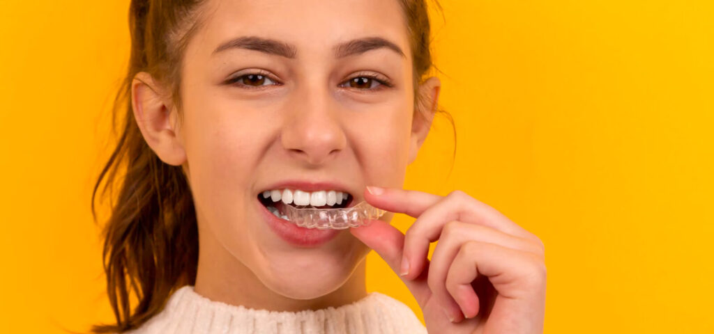 teen holds Invisalign tray between teeth as she learns Invisalign tips